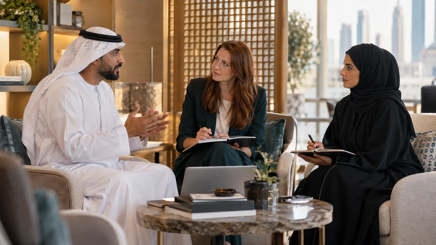 زميلتان تدوّنان الملاحظات بينما يتحدث زميل ثالث، في جلسة حول طاولة رخامية منخفضة.